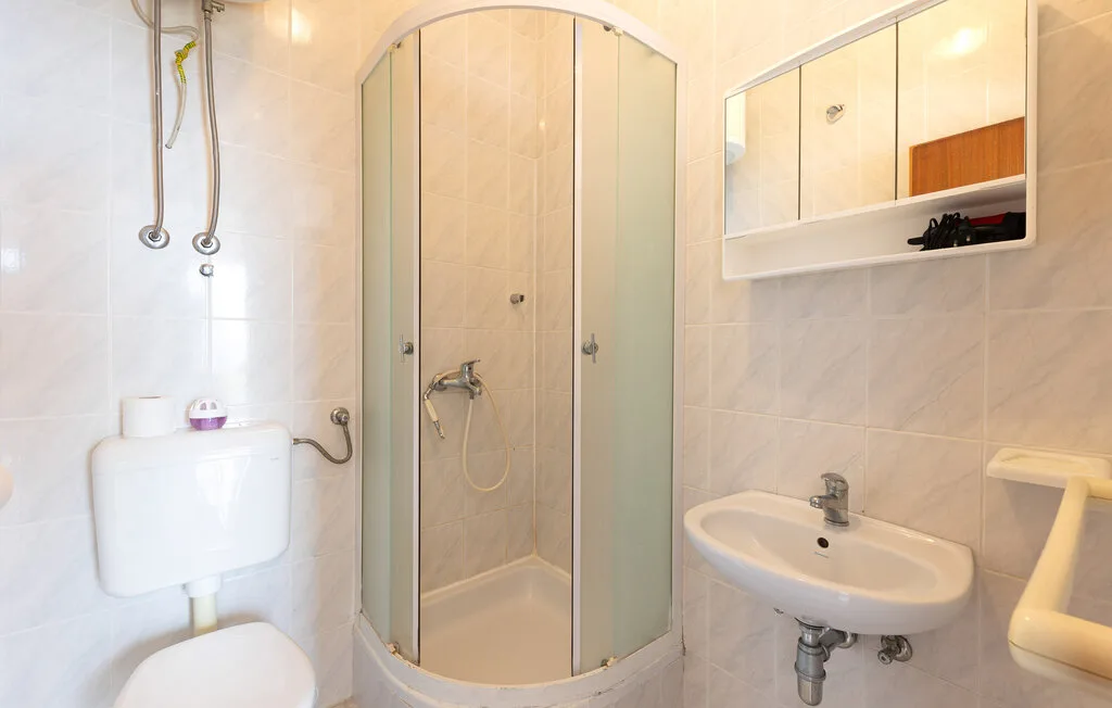 Un baño alicatado con una ducha de vidrio curvada y un lavabo de pared.