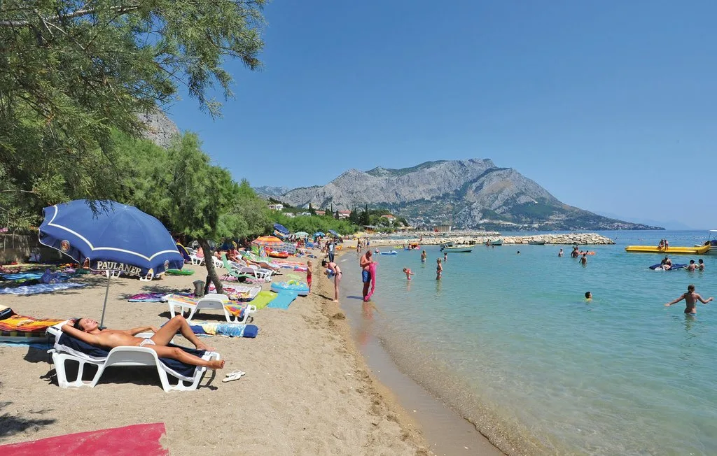 Una playa de arena tiene tumbonas junto a aguas tranquilas y montañas a lo lejos.