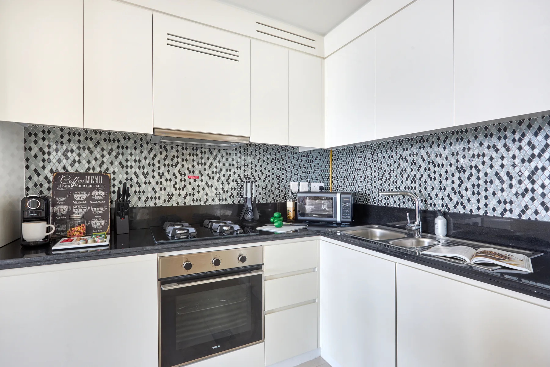 A modern kitchen with white cabinets, a dark countertop, and patterned backsplash.