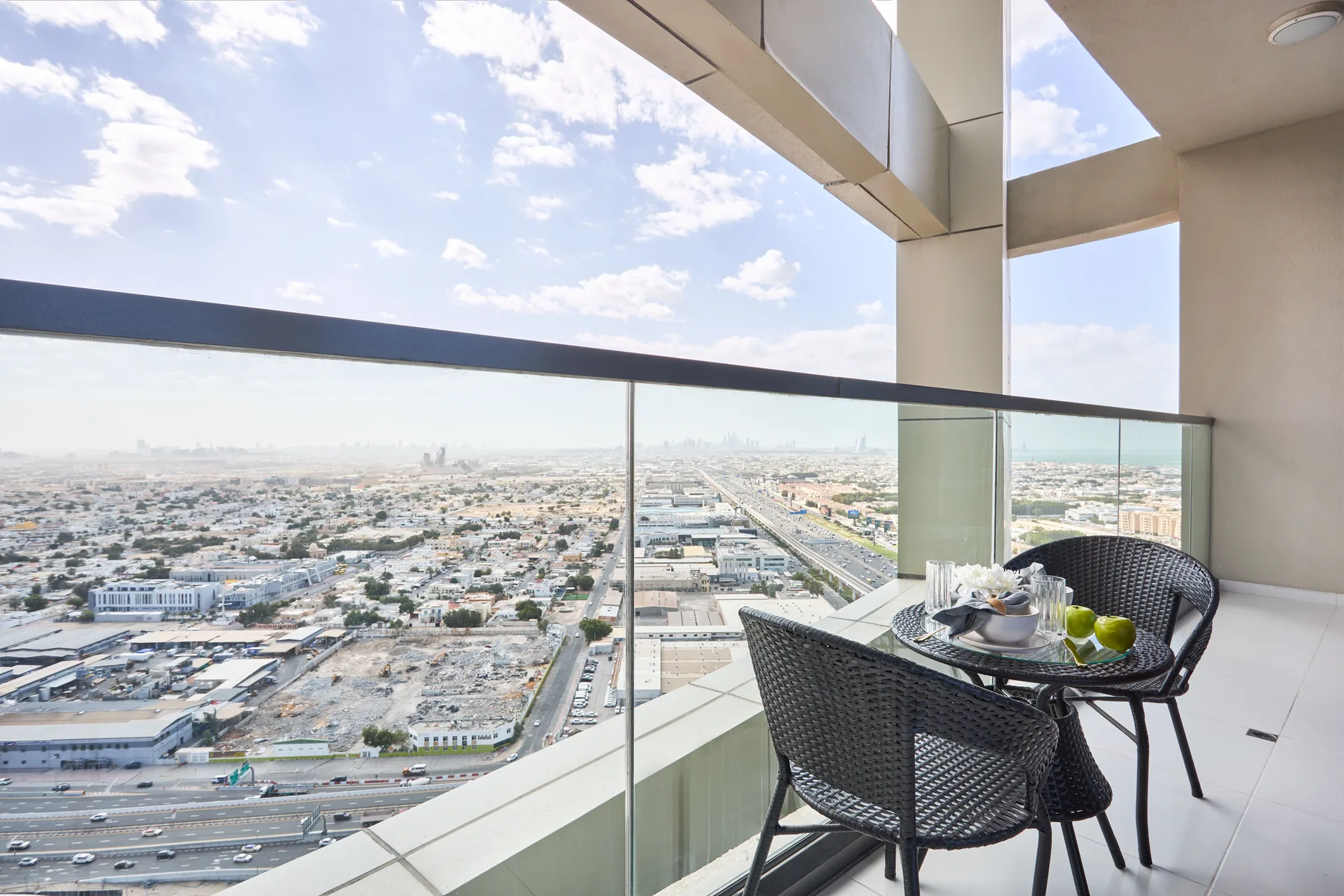 A high-rise balcony with seating and a table overlooks the city.