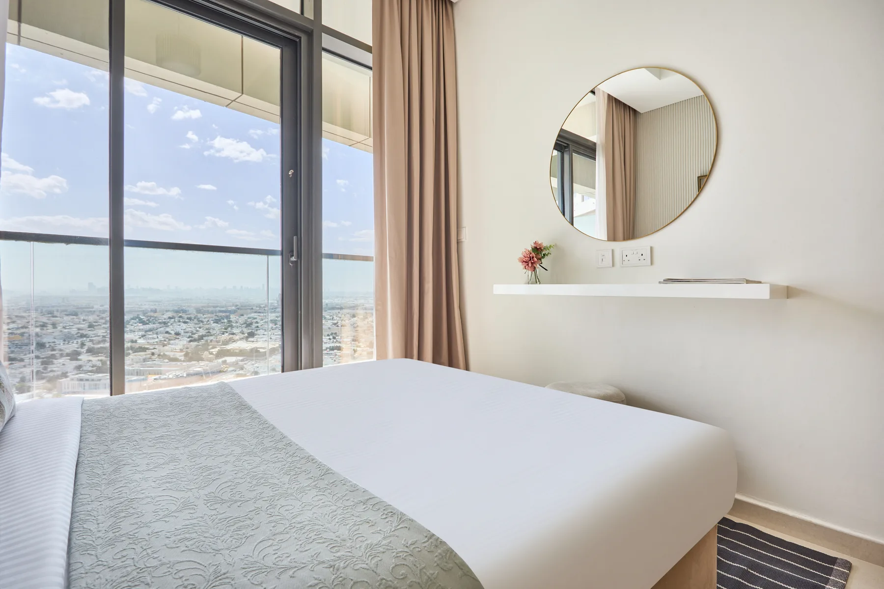 A bedroom with a bed beside floor-to-ceiling windows overlooking the city.