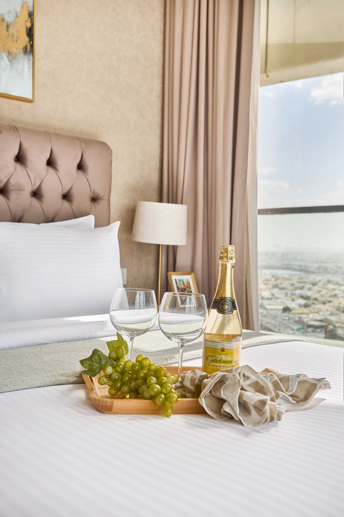 A bedroom with a bed, grapes, and a bottle of sparkling wine beside a window.