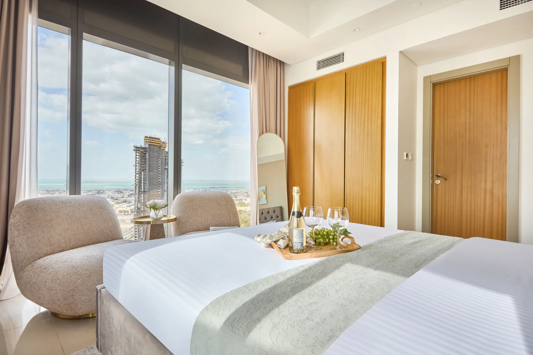 A bright bedroom with beds beside large windows overlooking the sea.