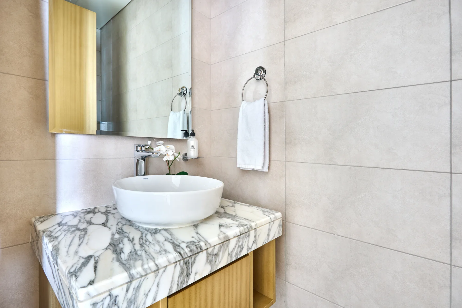 A bathroom vanity with a white basin, marble-patterned counter, and tiled walls.