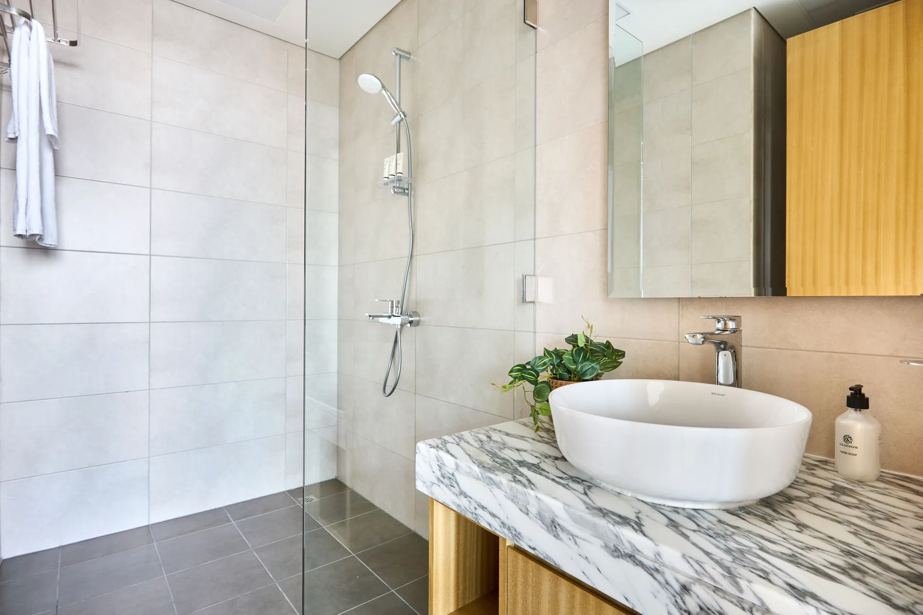 A tiled bathroom features a glass shower and a vessel sink on a stone counter.