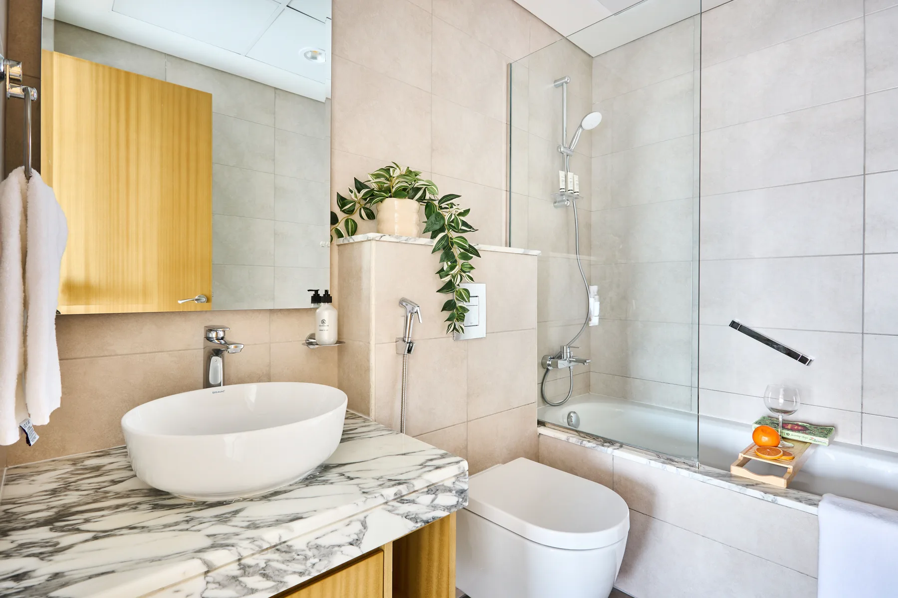 A bright tiled bathroom with a vessel sink, toilet, and glass shower.