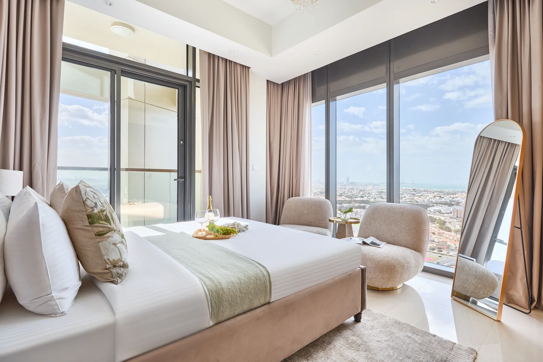 A bright bedroom with a bed beside large windows overlooking the city.