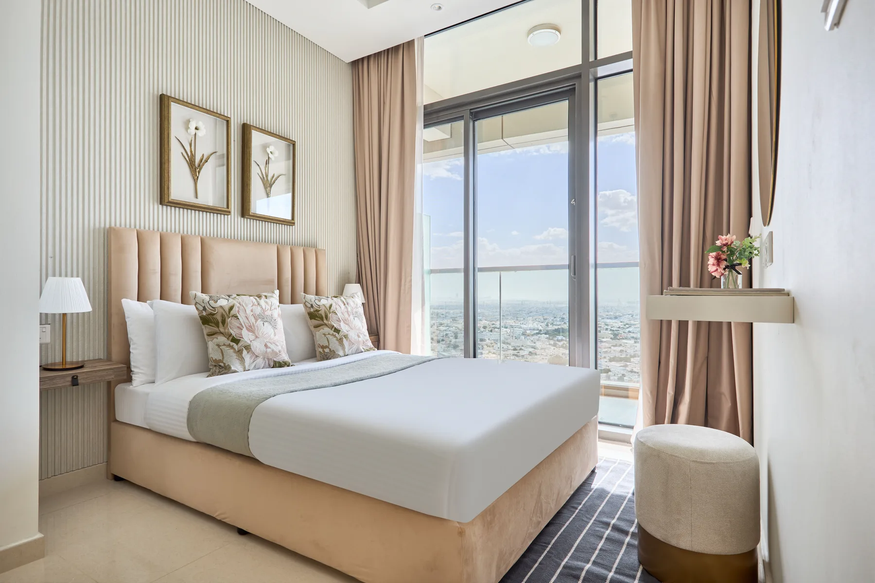 A bright bedroom with a large bed beside floor-to-ceiling windows.