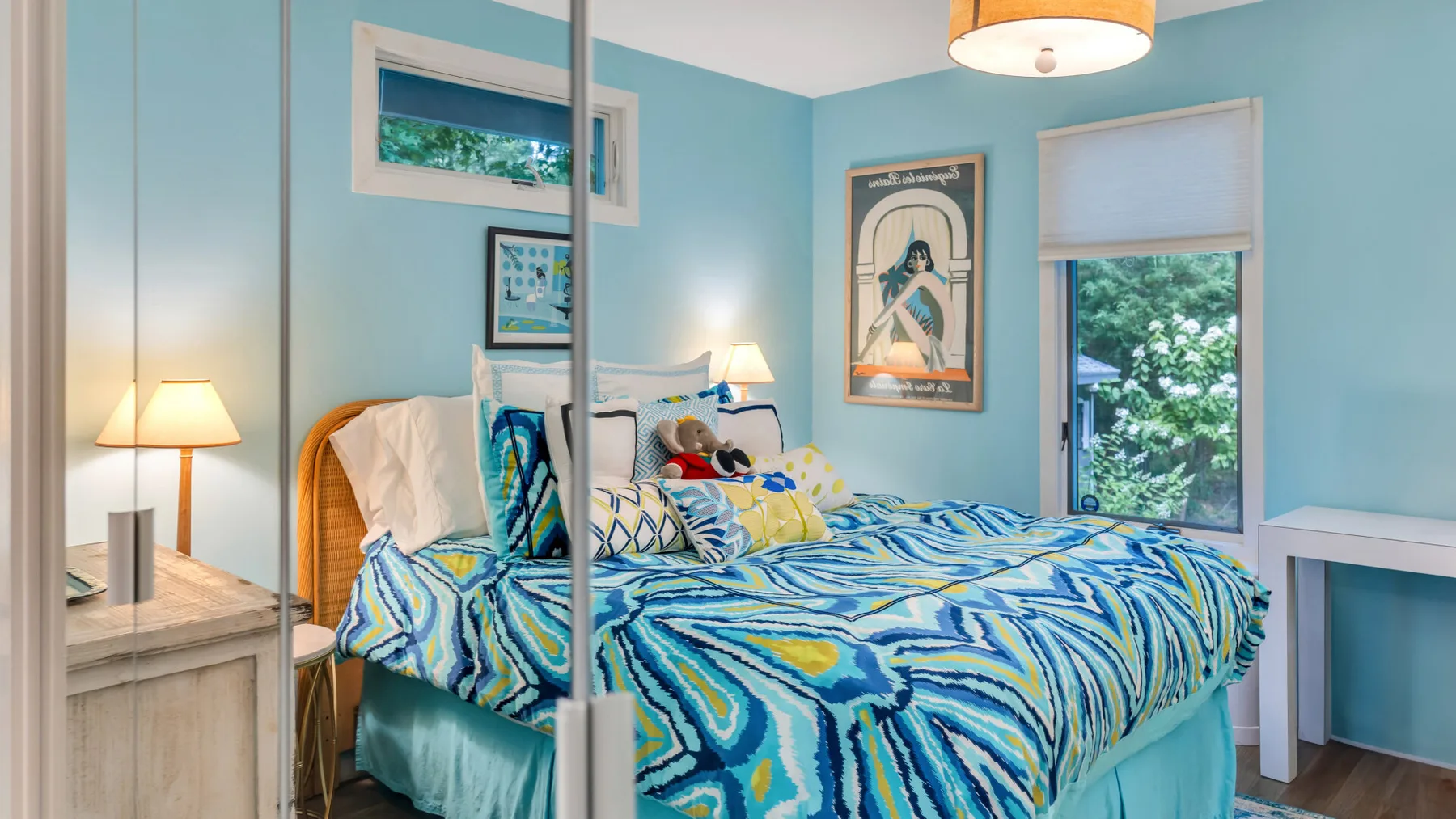 Un dormitorio luminoso con una cama cubierta con una colcha azul estampada.