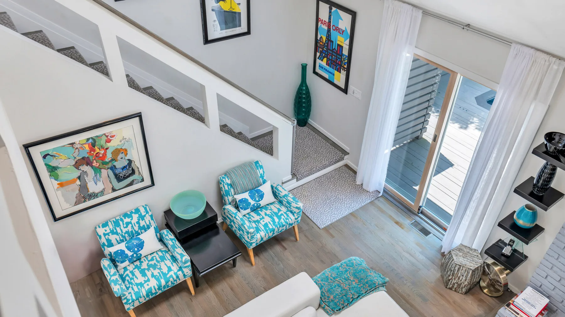 Una sala luminosa tiene asientos estampados junto a una escalera y puertas corredizas de vidrio.