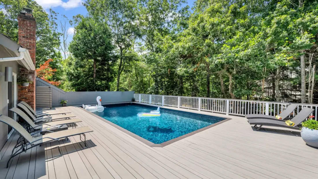 Una piscina al aire libre está junto a una amplia terraza rodeada de árboles.