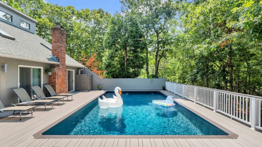 Una piscina al aire libre junto a una casa, con asientos y árboles.