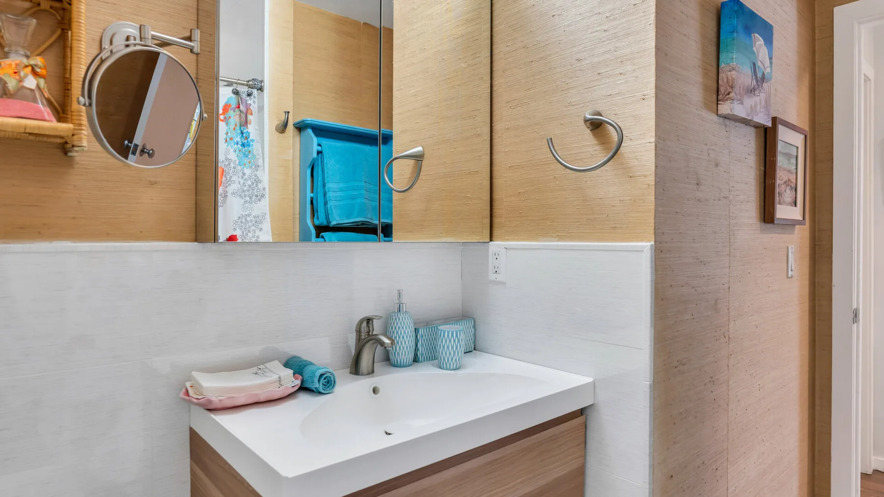 Un lavabo de baño con un fregadero blanco, armarios con espejo y un toallero de pared.