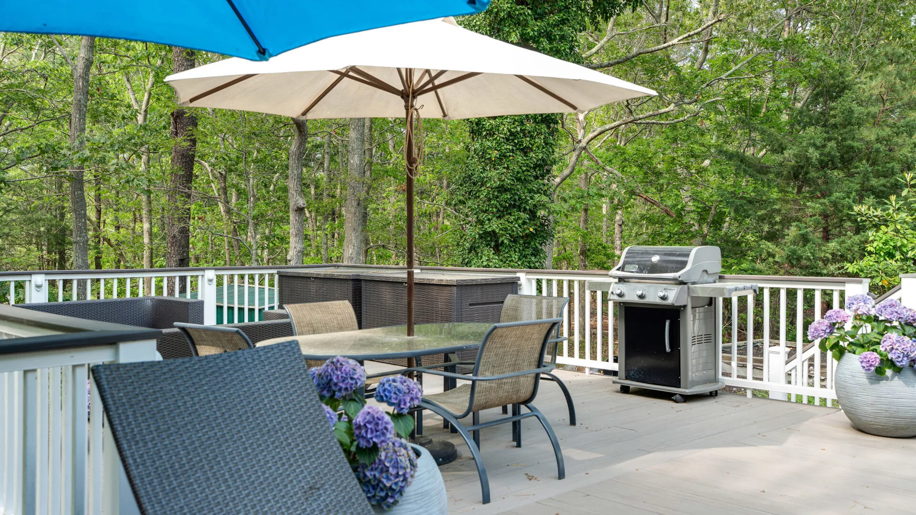 Una terraza exterior tiene una mesa de comedor, asientos, una sombrilla y una parrilla.