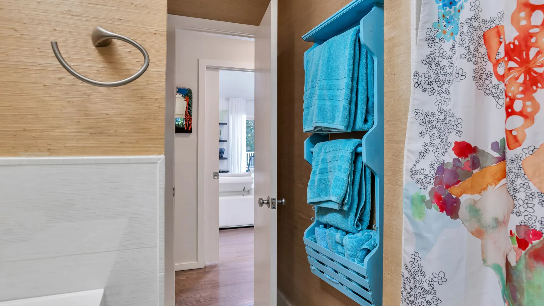Una puerta de baño da a otra habitación, junto a toallas turquesas en un estante.