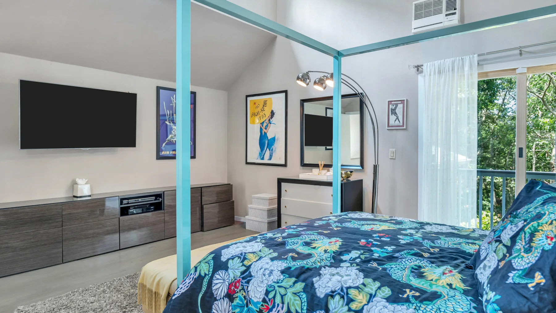 Un dormitorio con una cama estampada y colorida, un televisor de pared y puertas de vidrio al balcón.