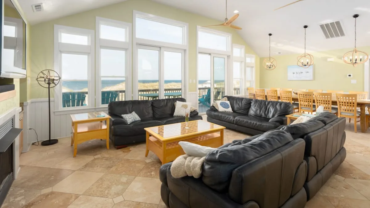 A bright open-plan living and dining area with dark seating and a wooden dining table.