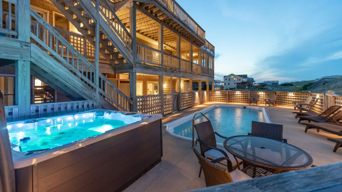 Una piscina exterior iluminada junto a un edificio de madera de varios niveles y asientos de patio.