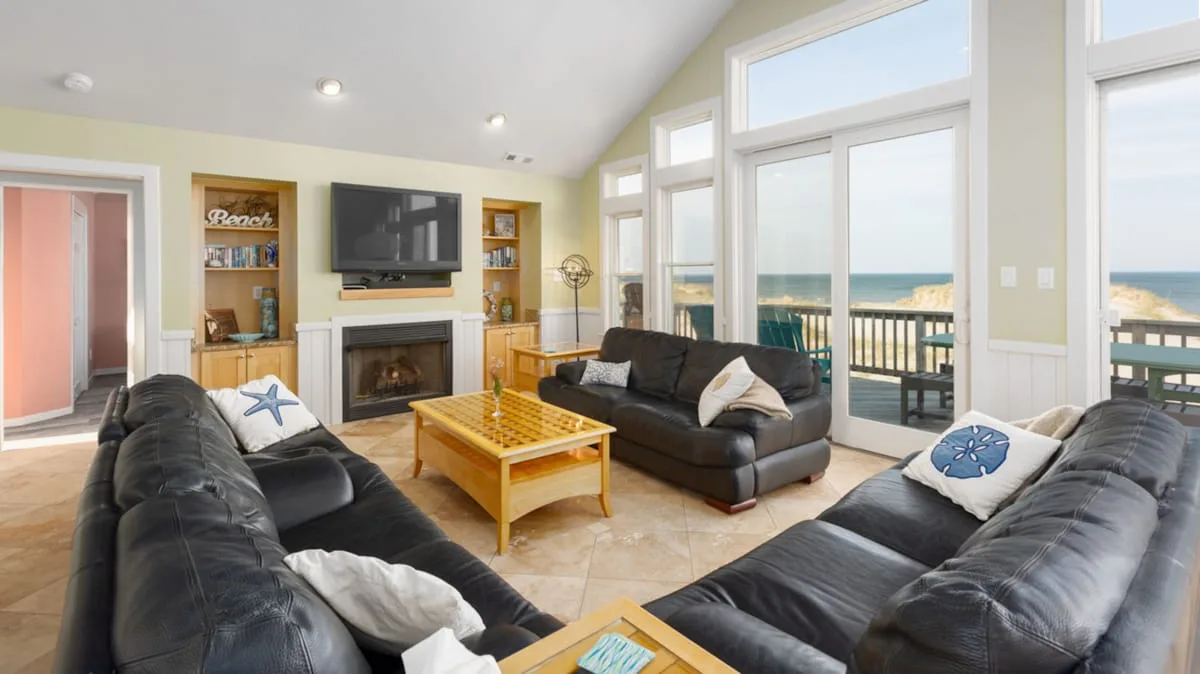 A bright living room has leather seating, a fireplace, and wide windows overlooking the water.