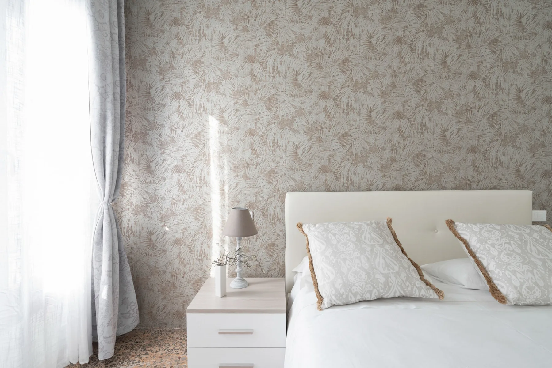 A bedroom with a bed beside a white nightstand and bright window.