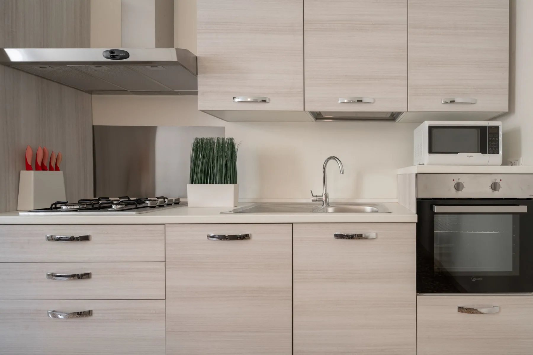 A modern kitchen with pale cabinetry, a cooktop, sink, and built-in appliances.