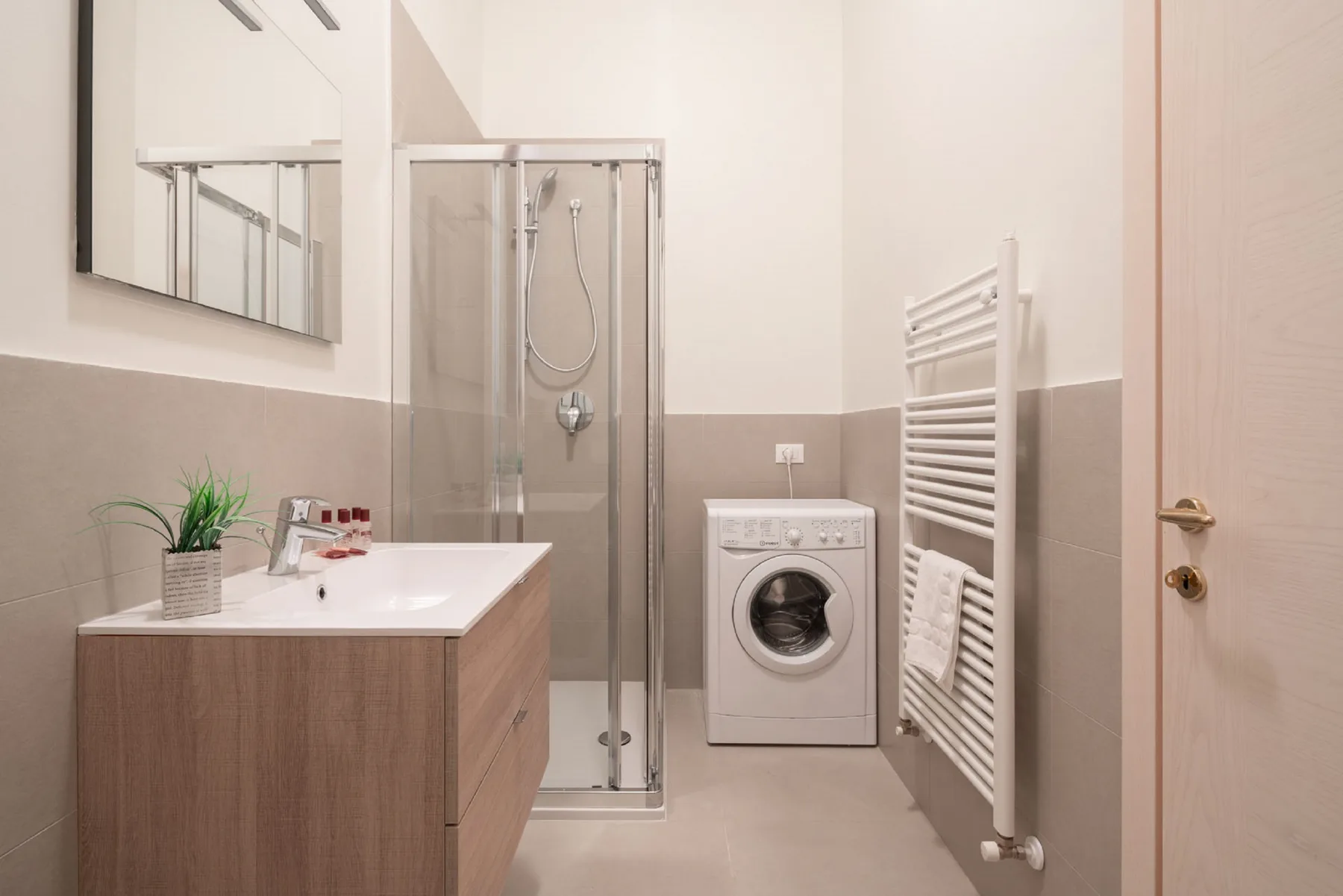 A bathroom with a sink, shower, washing machine, and towel warmer.