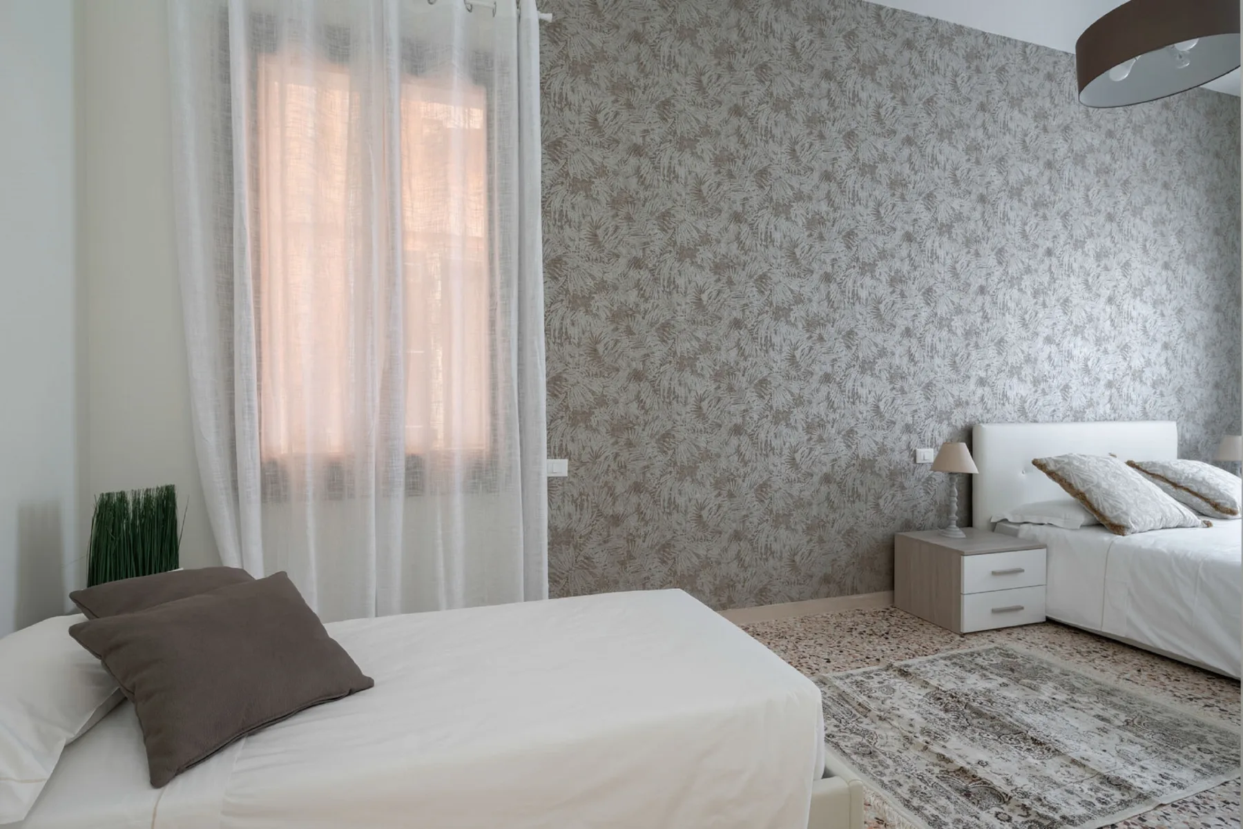 A bedroom with two beds, patterned wallpaper, and a rug.