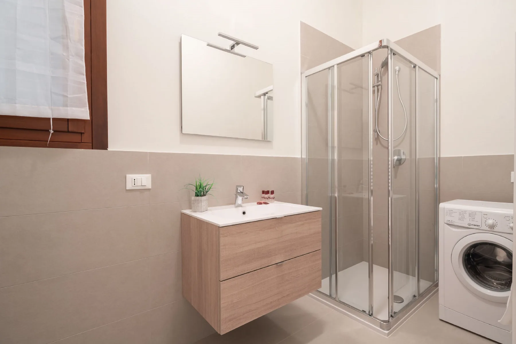 A bathroom with a glass shower, floating vanity, and washing machine.