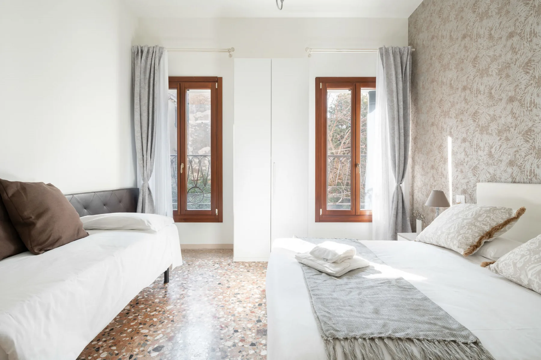 A bright bedroom with two beds and tall windows.