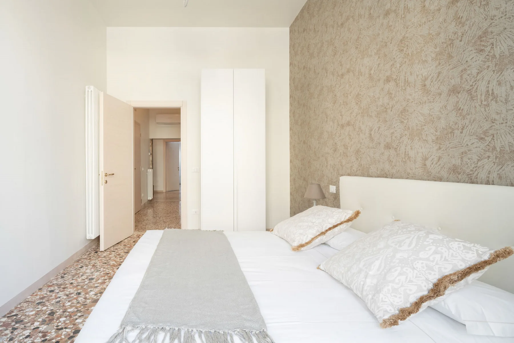 A bedroom with a bed, patterned accent wall, and white wardrobe.