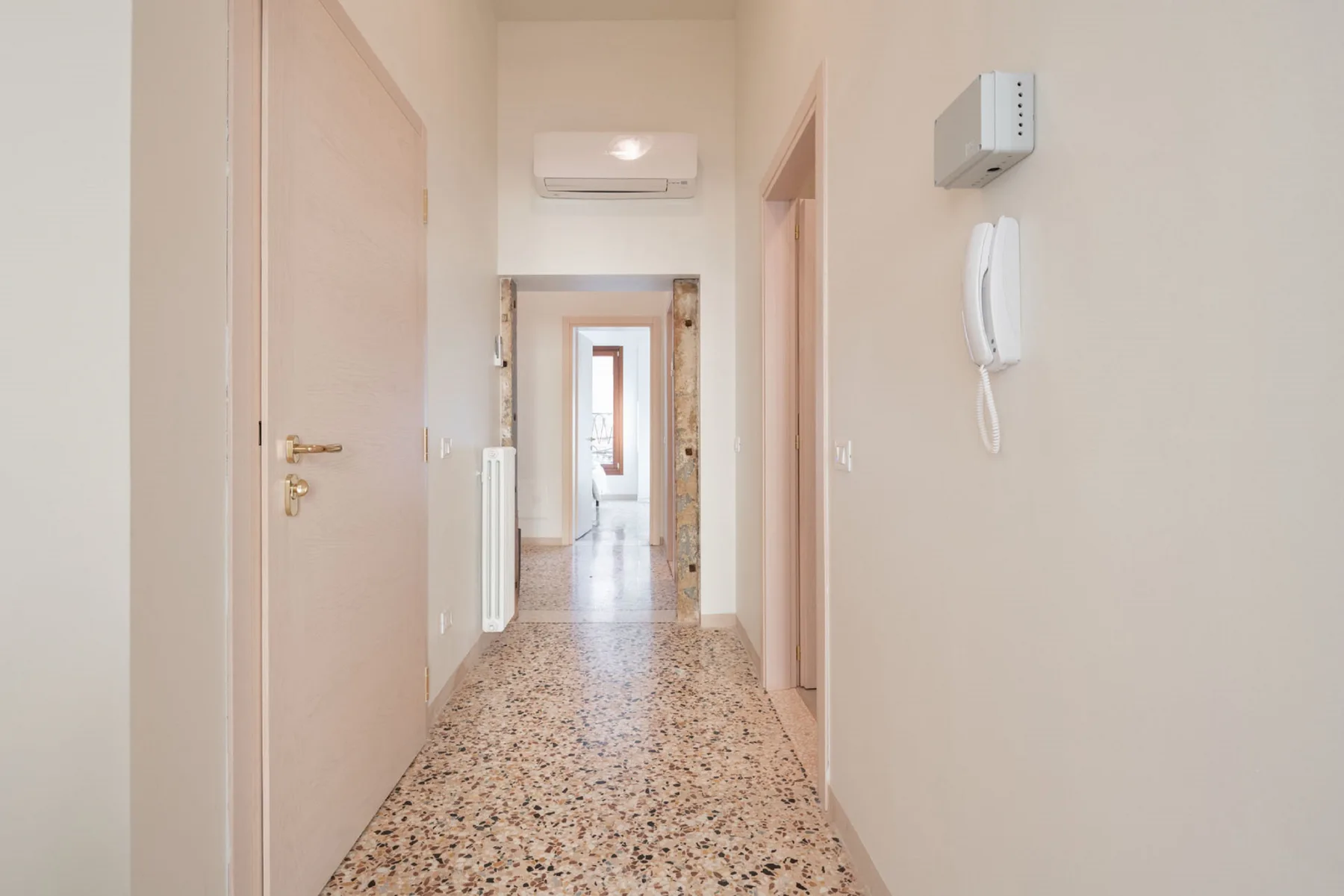 A bright hallway with a terrazzo floor and doors along the corridor.