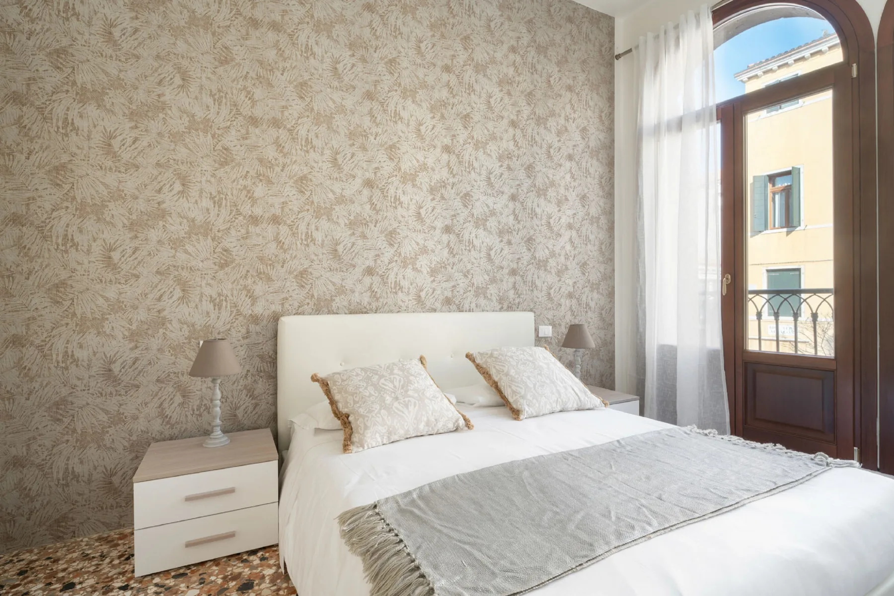A bedroom with a white bed beside a tall arched window.