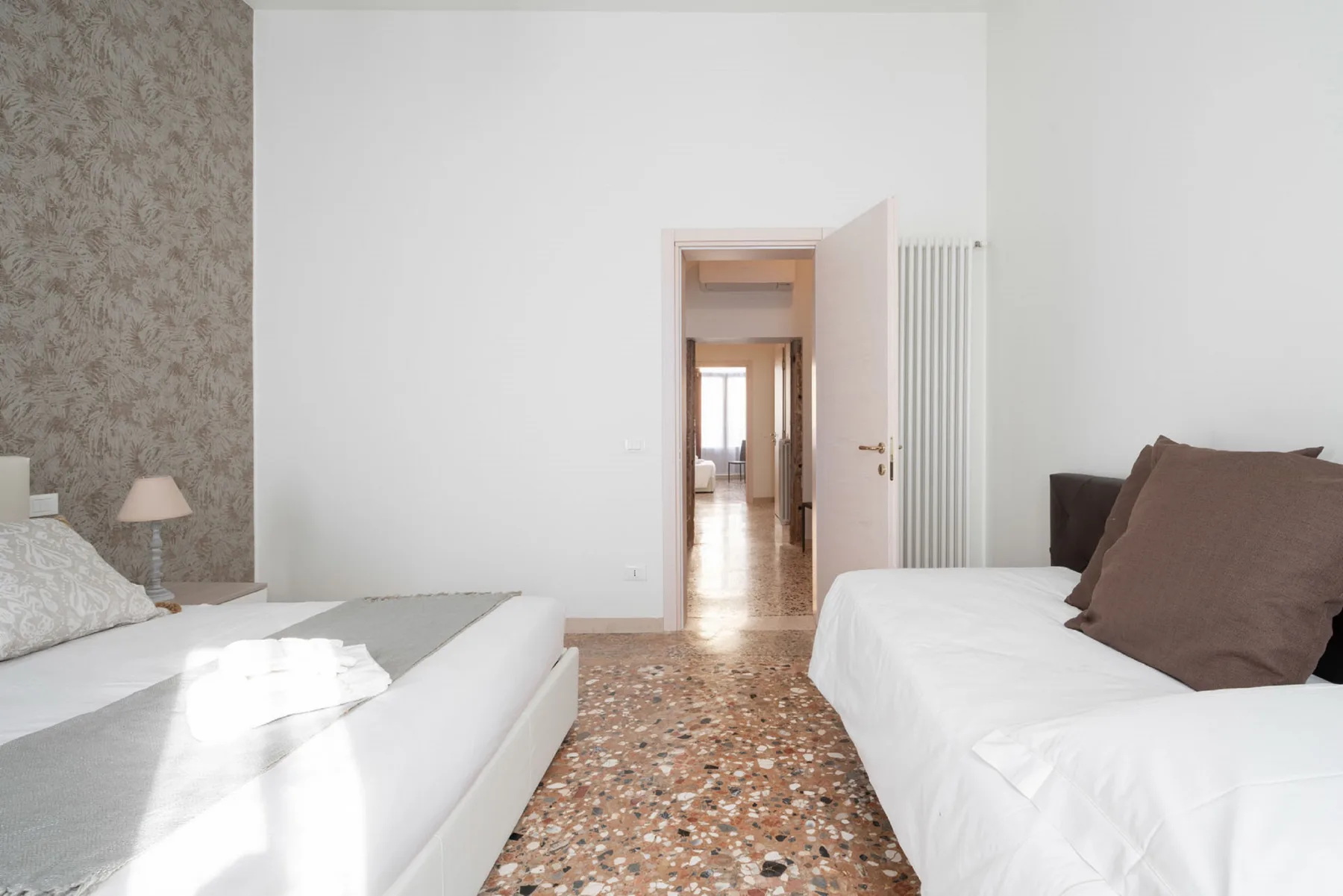 A bright bedroom with two beds and an open doorway leading to a hallway.