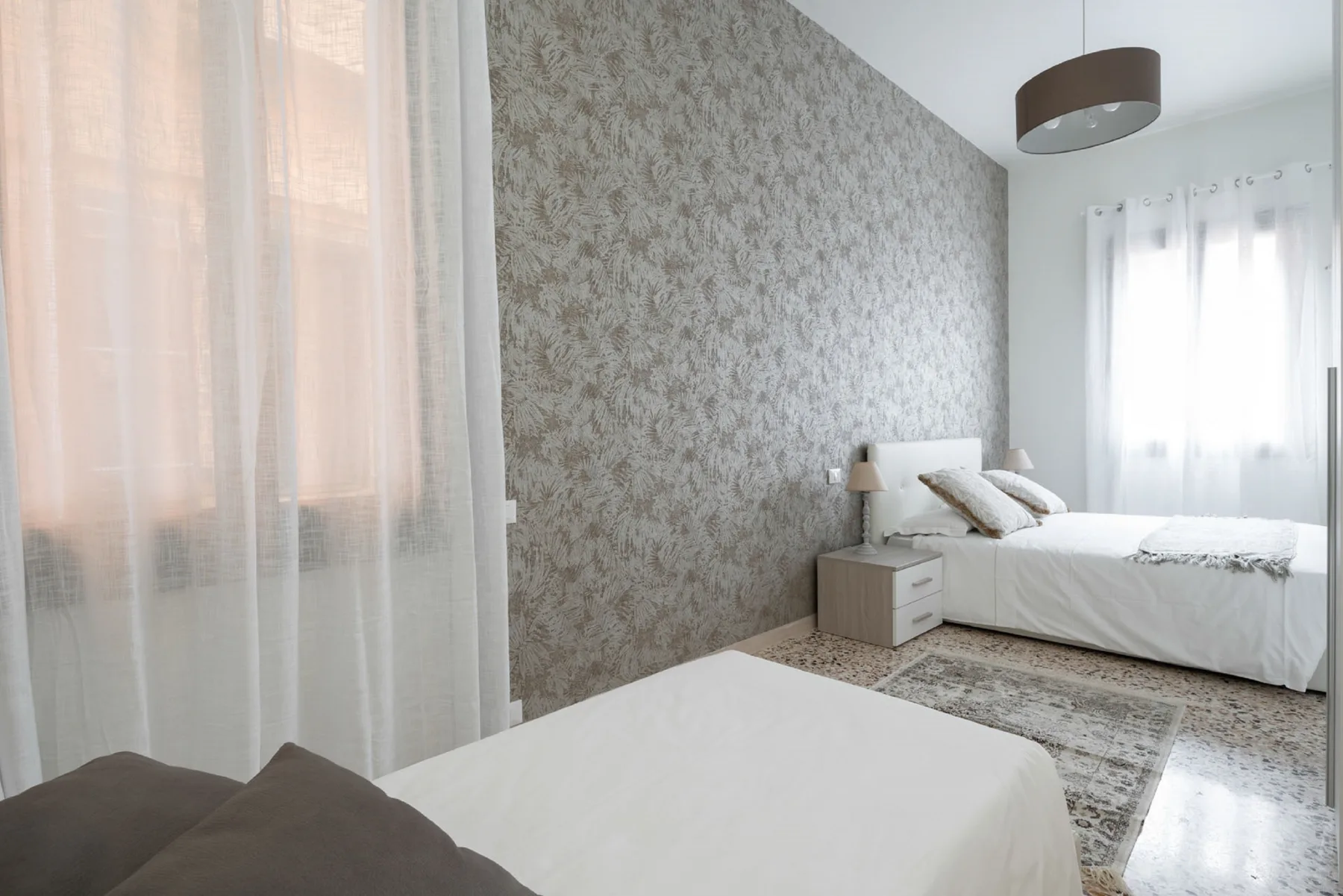 A bright bedroom with white bedding and sheer curtains.