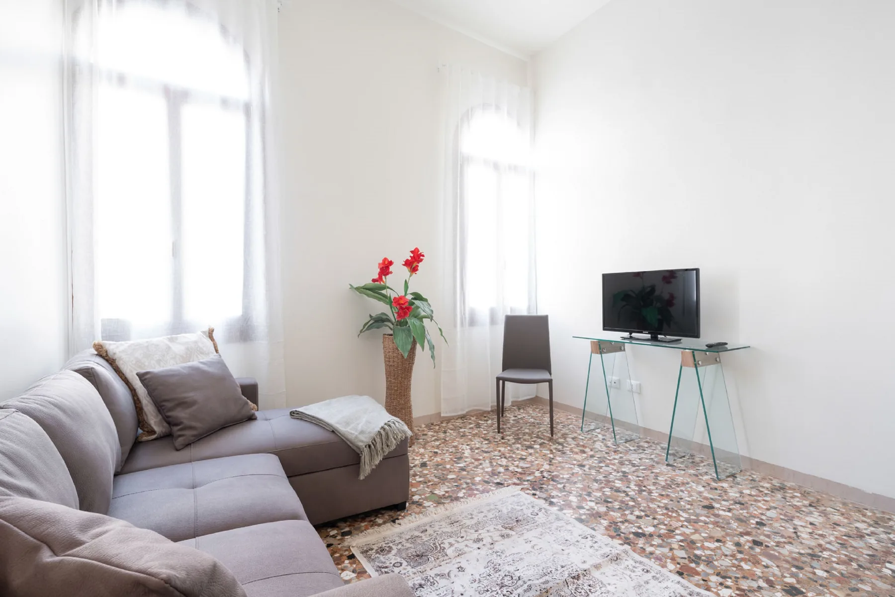 A bright living room with seating, a television, and tall windows.