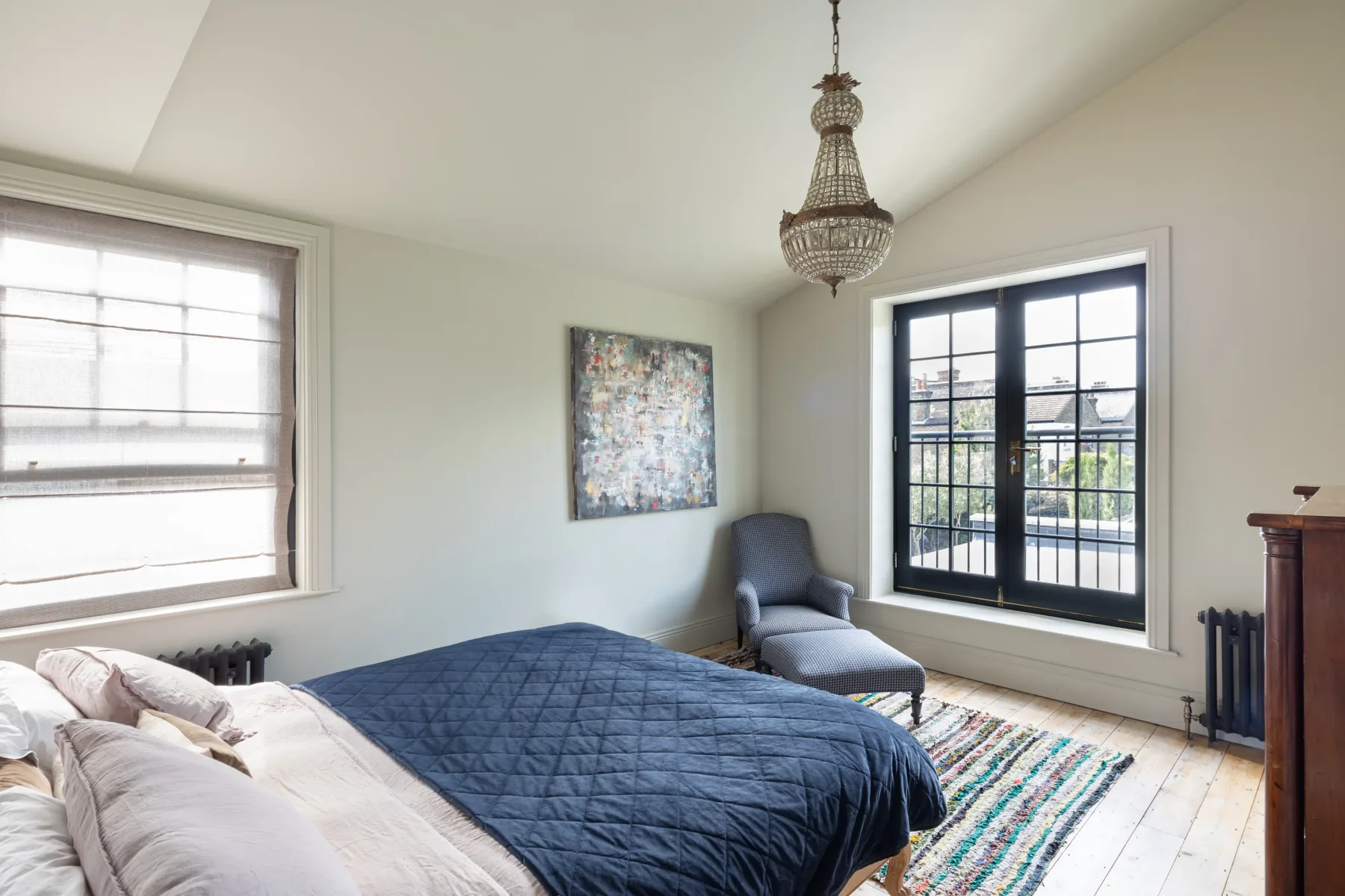 A bright bedroom with a bed, an armchair, and large windows.