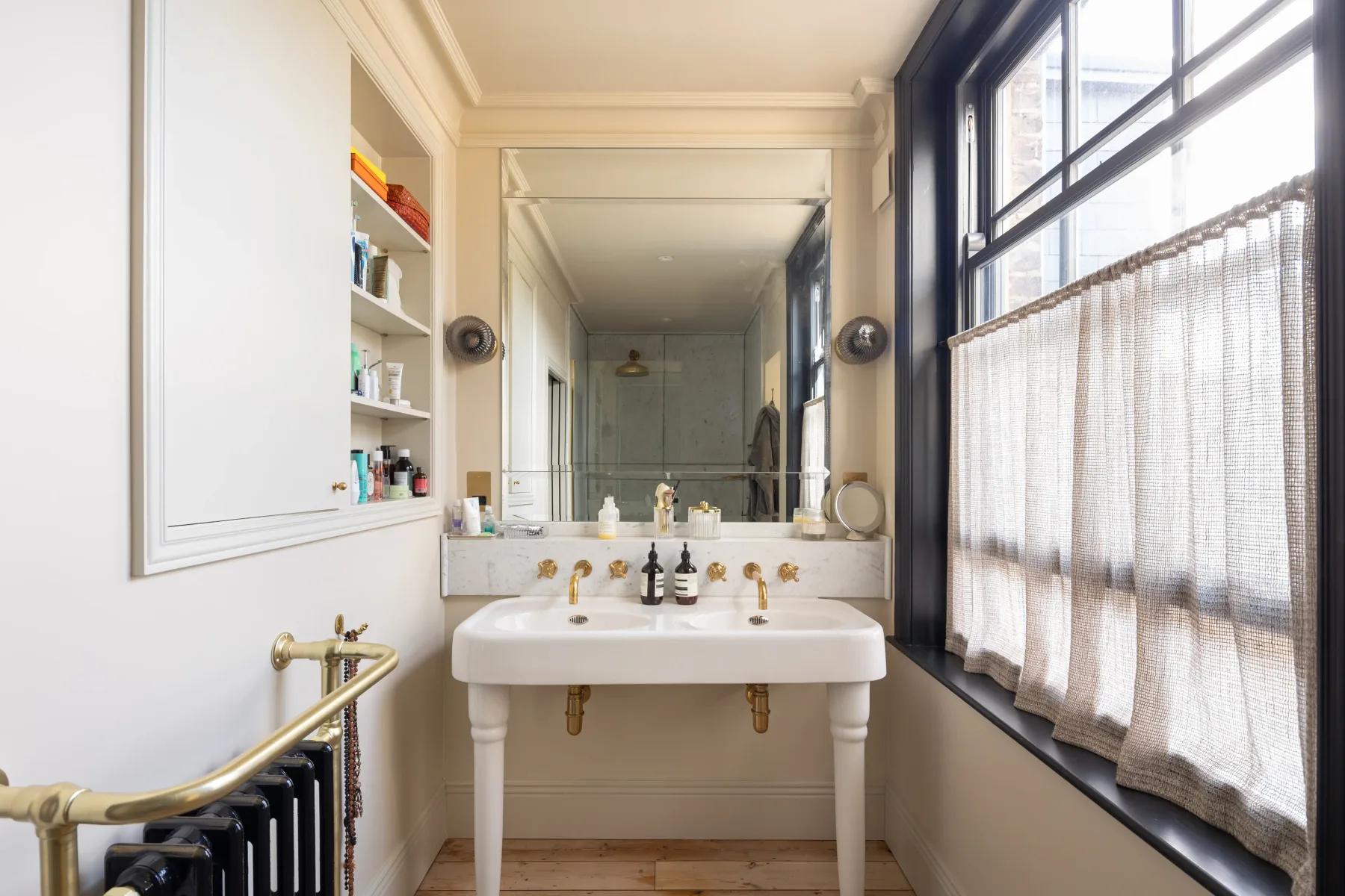 Un baño luminoso con lavabo de pedestal, espejo grande y ventanas altas.