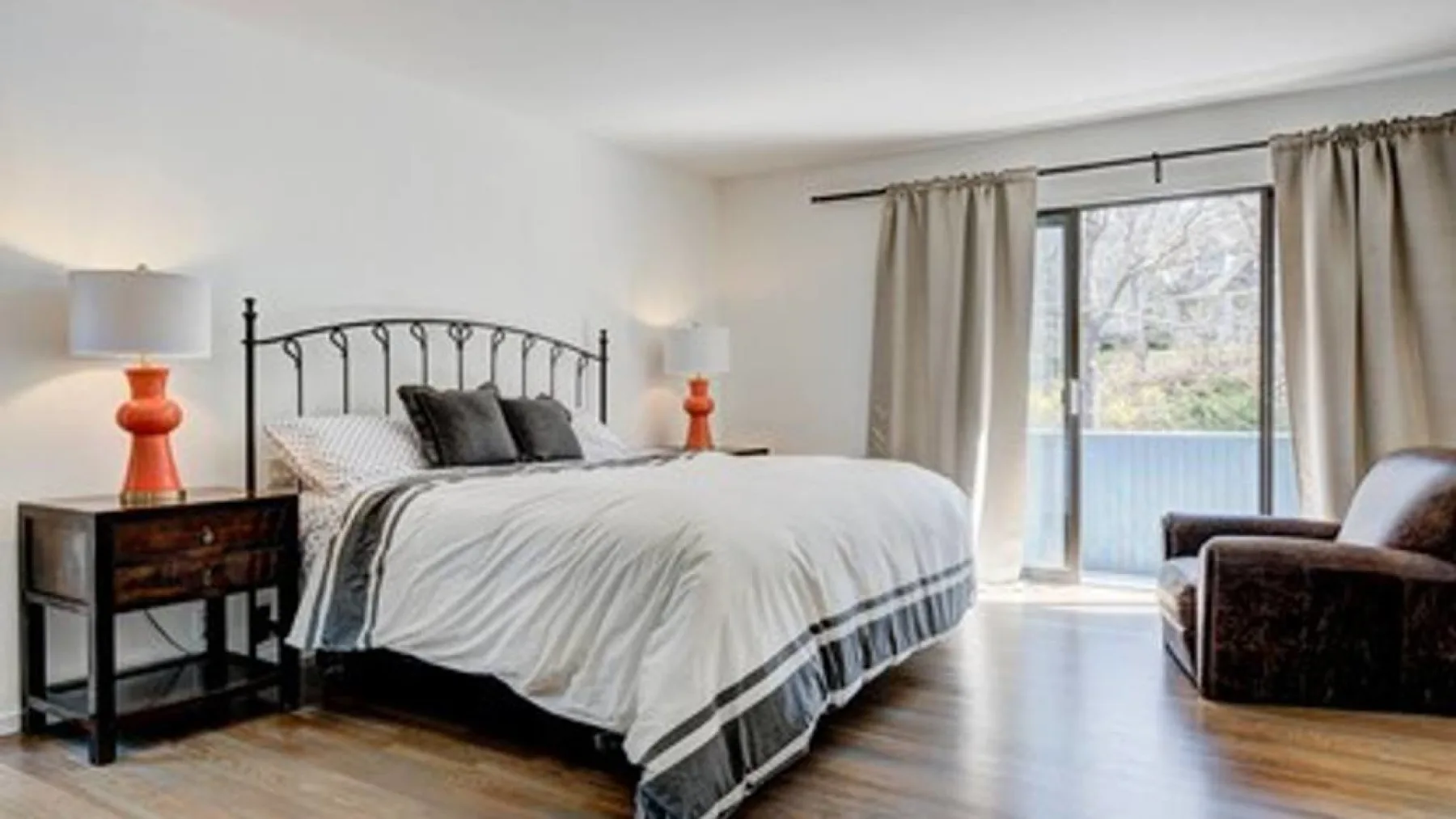 Un dormitorio con una cama grande, mesitas de noche y cortinas junto a una puerta de vidrio.