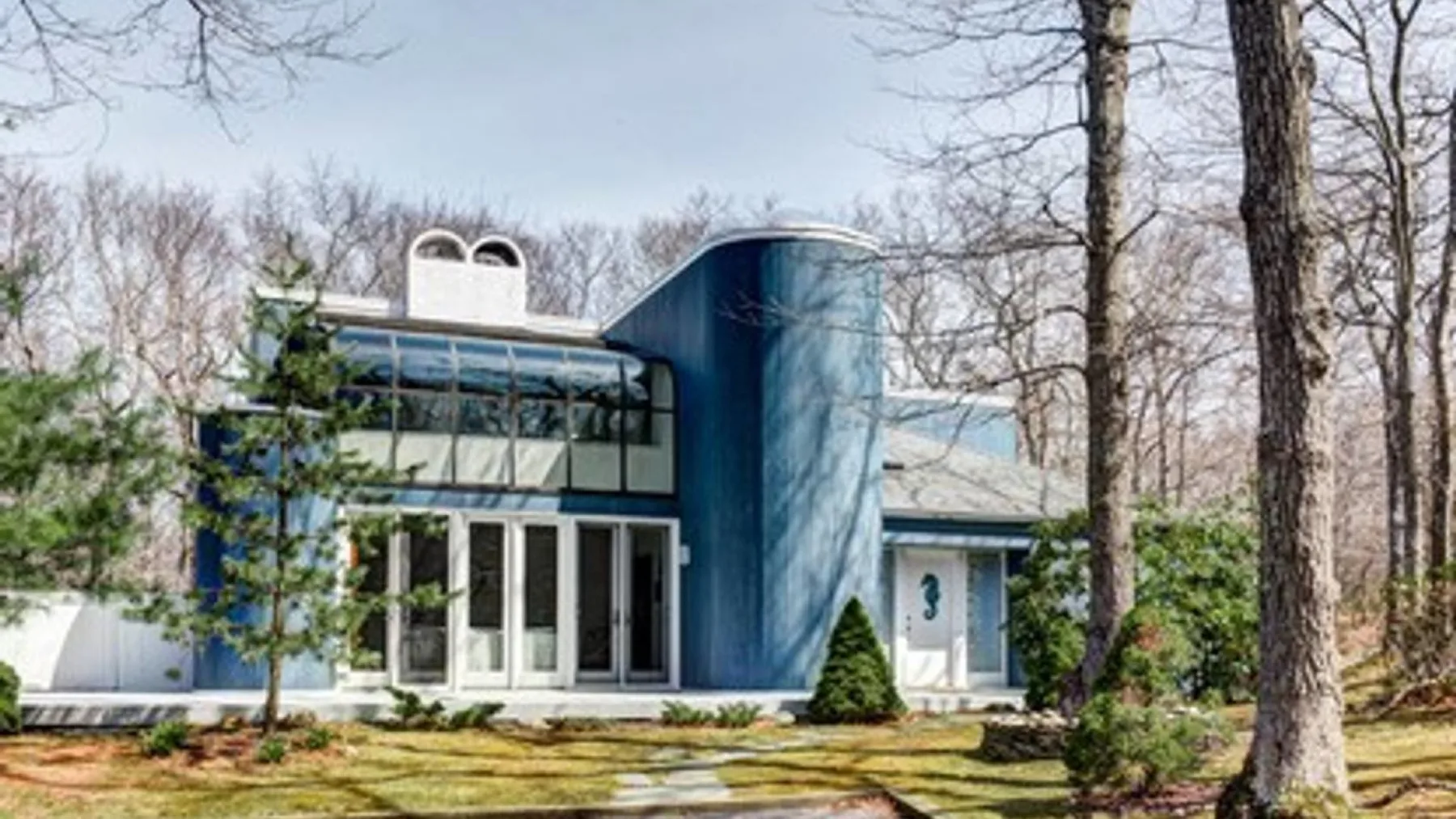 A modern house with large windows stands among leafless trees.