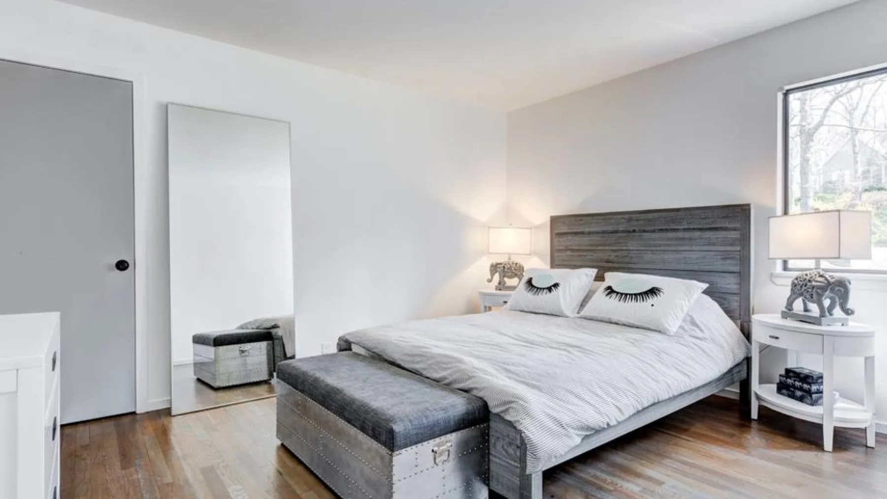 Un dormitorio luminoso con una cama, mesitas de noche y un espejo grande.