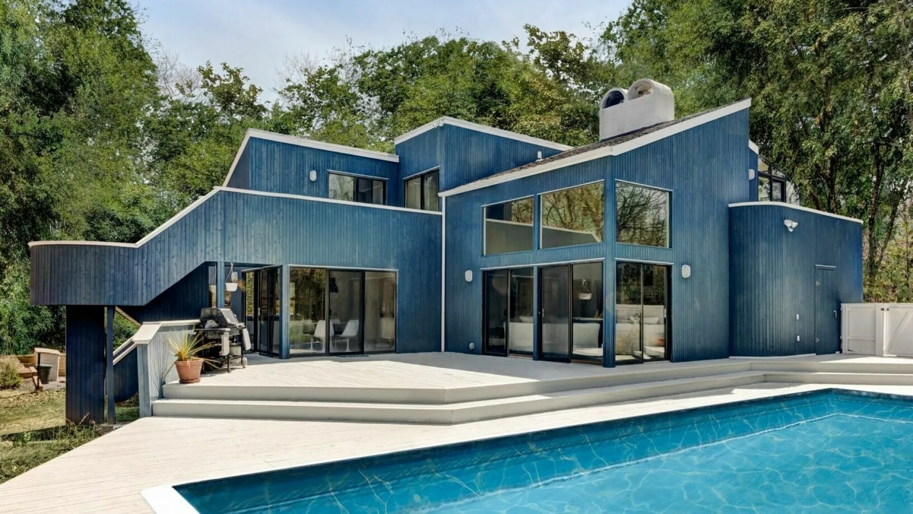 A blue modern house stands beside a swimming pool, with a broad patio.