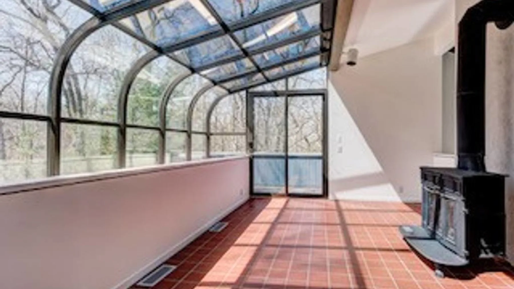 Un solárium con techo curvo de vidrio y grandes ventanas con vistas a los árboles.