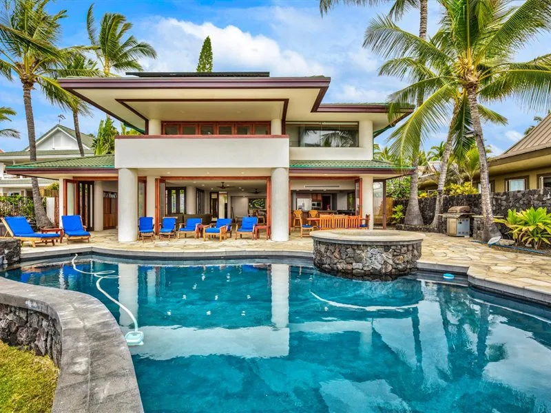 Un edificio tropical da a una piscina con asientos junto al patio.