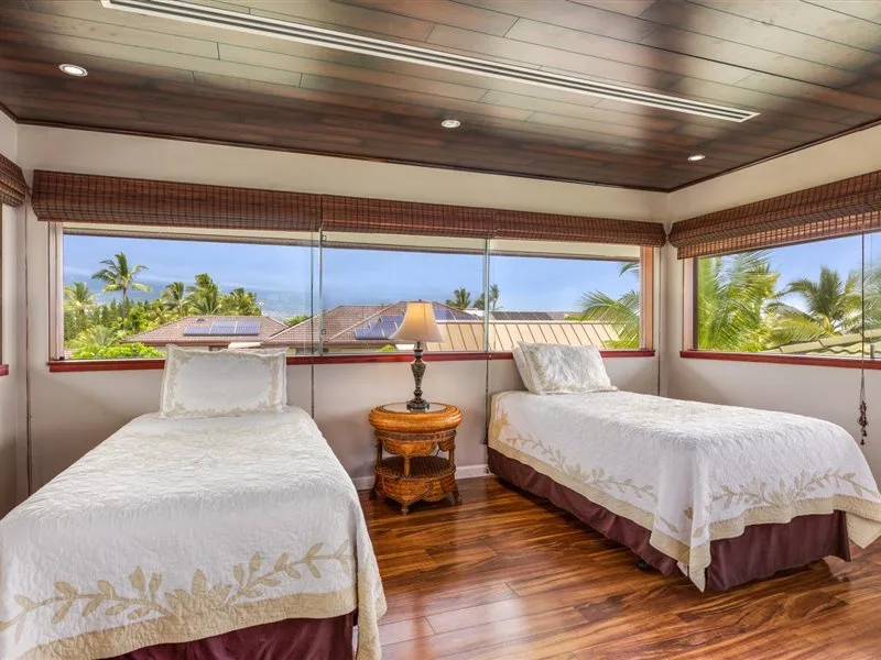 Un dormitorio con dos camas junto a amplias ventanas con vistas a vegetación tropical.
