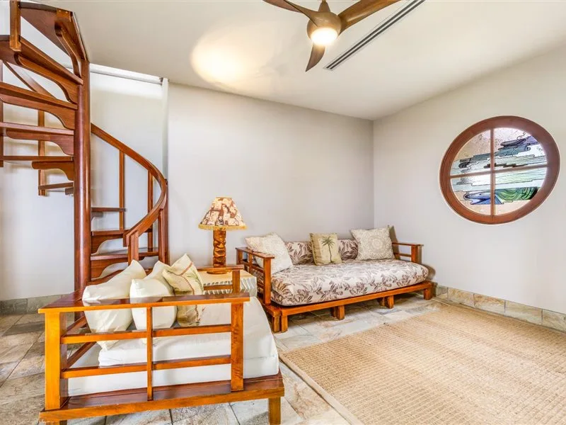 Una sala de estar con asientos de madera, un sofá estampado y una escalera curva.