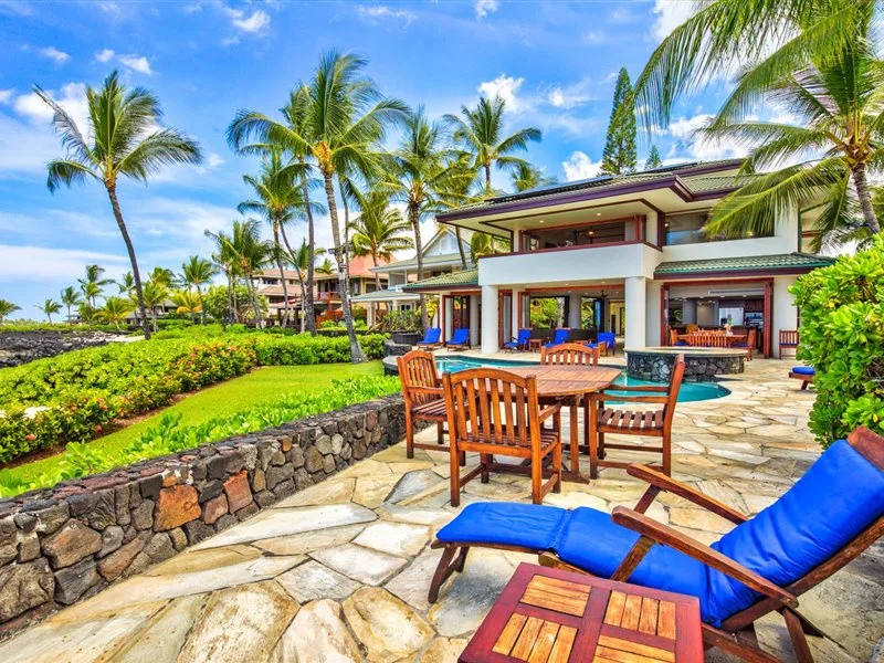 Un patio tropical al aire libre con asientos de madera junto a una piscina.