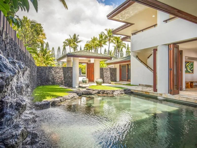 Un patio de villa moderna con piscina, plantas tropicales y elementos de agua de piedra.
