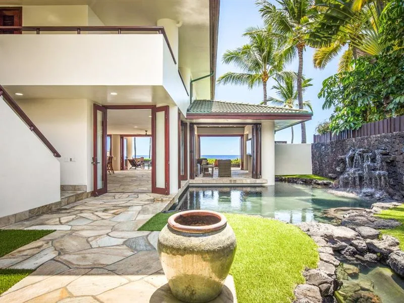 Un patio tropical con piscina, pavimento de piedra y palmeras.