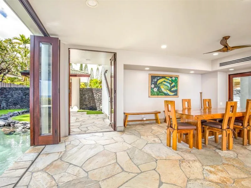 Un comedor abierto con mesas y sillas de madera junto a un patio pavimentado de piedra.
