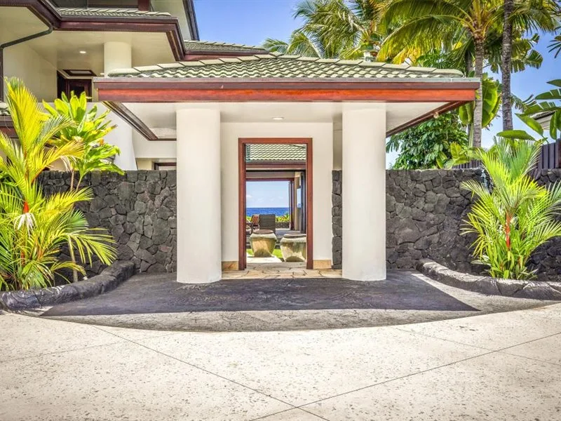 La entrada de una villa, enmarcada por muros de piedra y plantas tropicales.